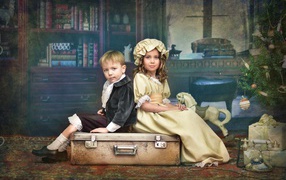 Маленькие мальчик и девочка в винтажных костюмах сидят на чемодане