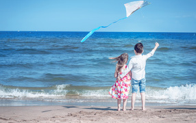 Маленькие мальчик и девочка запускаю воздушного змея на пляже