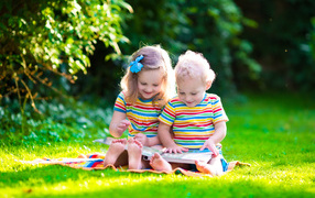 Маленькие мальчик и девочка читают книгу сидя на зеленой траве
