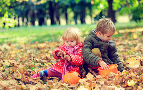 Маленькие мальчик и девочка сидят на желтой листве в парке осенью