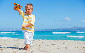 Маленький мальчик на пляже с игрушечным самолетом в руках