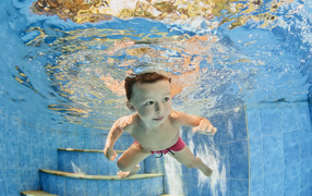 Маленький мальчик плавает под водой в бассейне