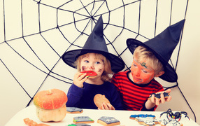 Маленькие дети в костюмах на Хэллоуин едят праздничные сладости