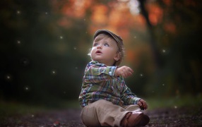 Маленький милый мальчик сидит в кепке на дороге