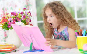 Little fair-haired girl looks at the book in surprise