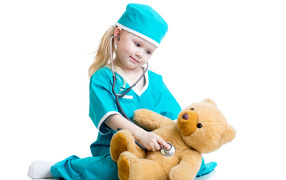 Little girl dressed as a doctor treats a teddy bear