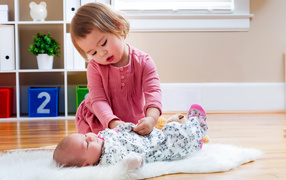 Маленькая девочка одевает грудного младенца