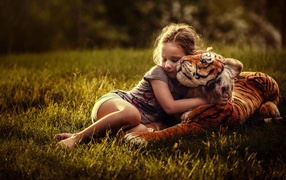 Little girl hugging a toy tiger on a green grass
