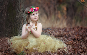 Маленькая девочка в красивом платье сидит на сухой листве