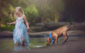 Маленькая девочка в красивом платье со щенком у ручья