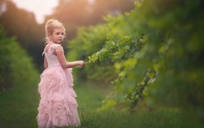 Маленькая девочка в красивом розовом платье стоит на зеленой траве