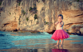 Маленькая девочка в красивой розовой юбке на пляже