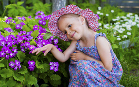 Маленькая девочка в шляпе рядом с фиолетовыми цветами