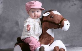 Маленькая девочка в розовой кепке сидит на игрушечной лошади