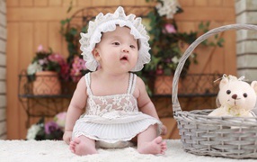 Маленькая девочка в белом платье с медвежонком в корзине