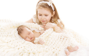 Маленькая девочка в белом со спящим младенцем на белом фоне