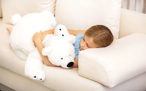 Little girl is sleeping with a white teddy bear on the couch