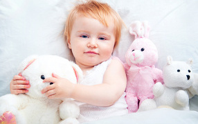 Little girl lies in bed with plush toys