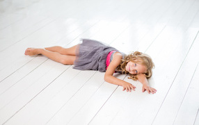 Little girl model in a gray dress lies on a wooden floor