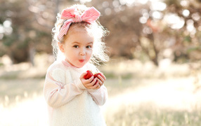 Маленькая девочка с бантом на голове ест клубнику