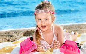 Маленькая девочка с голубыми глазами загорает на пляже