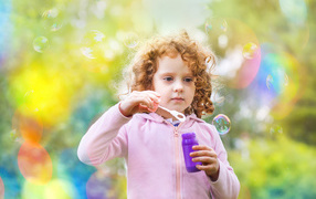 Little red-haired curly girl with soap bubbles