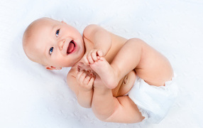 Маленький улыбающийся грудной ребенок держит руками ноги