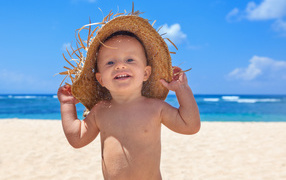 Маленький улыбающийся мальчик в соломенной шляпе на пляже