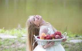 Маленькая улыбающаяся девочка в белом платье с корзиной фруктов