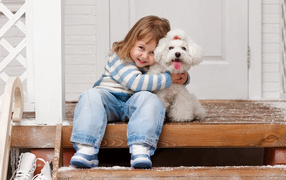 Little smiling girl sitting with a white poodle on the steps