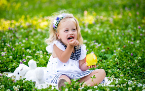 Маленькая улыбающаяся девочка с яблоком сидит на зеленой траве