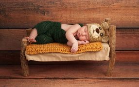 Newborn baby in a bear's costume sleeps on a tiny bed