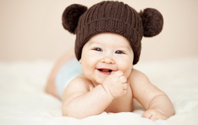 Улыбающийся грудной ребенок в коричневой вязаной шапке