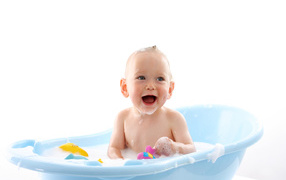 Улыбающийся грудной ребенок сидит в синей ванночке на белом фоне