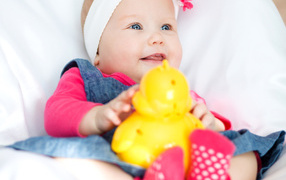 Улыбающаяся голубоглазая девочка младенец с игрушкой в руках