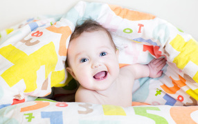 Улыбающийся голубоглазый ребенок под разноцветным покрывалом