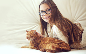 Улыбающаяся девочка шатенка в очках гладит рыжего кота