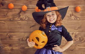 Smiling little girl in a witch costume with pumpkin on Halloween