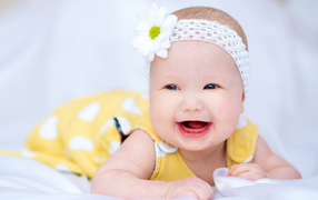 Улыбающаяся маленькая девочка в повязке с белым цветком на голове