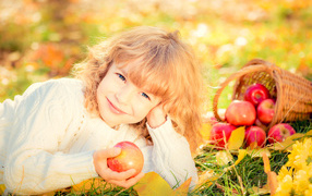 Улыбающаяся рыжеволосая девочка с корзиной красных яблок