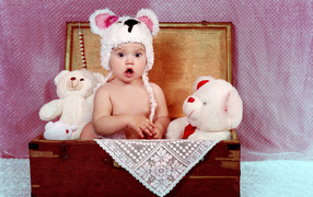 Удивленный малыш сидит в сундуке с мягкими игрушками