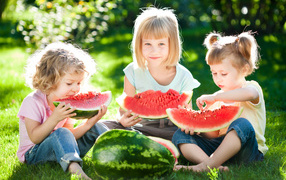 Три маленькие девочки едят арбуз на зеленой траве летом