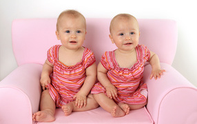 Две милые маленькие девочки сидят на розовом диване