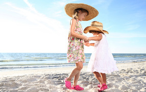 Two little girls are dancing in the sand on the beach