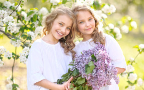 Two smiling girls twins with a bouquet of lilacs