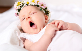 Зевающая маленькая девочка с венком из цветов на голове