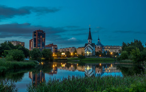 Вечерние огни маленькой церкви и домов отражаются в воде городского пруда, Санкт-Петербург. Россия