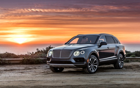Черный стильный стильный автомобиль Bentley на фоне заката 