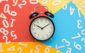 Будильник на разноцветном фоне с цифрами