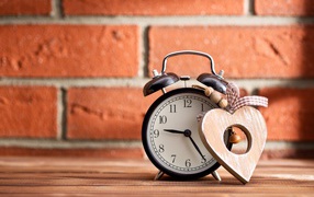 Будильник с деревянным сердцем стоит на фоне стены